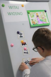 Uczeń przypinający do tablicy magnetycznej symbole wiosny.