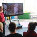 Prowadząca konkurs prezentująca uczniom owieczkę na tablicy multimedialnej.