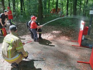 Ucznieiwe oraz strażacypodczas poazowej aktywności lania wodą z węża strażackeiego do celu.