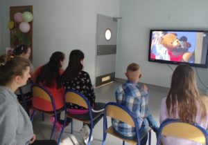Uczniowie oglądający teatr internatowy na tablicy multimedialnej.