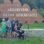 Grupa uczniów pozująca wplenerze na tle drewnianej dekoracji w kształcie liścia z napisem Arboretum Bramy Morawskiej.
