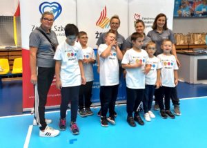 Grupa uczesników Dnia Młodych Sportowców pozująca nauczycielami, trenerami na tle rollupów z logotypami organiztora.