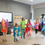 Grupa dziwczynek wraz z nauczycielką podczas wystepu - tańca z kolorowymi chustami.