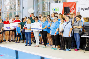 PrzedstawicieleProgramu Rodzinnego oraz zawodnicy podczas ceremonii otwarcia zawdoów nad niecką basenu.