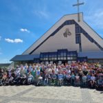 Zdjęcie grupowe podopiecznych oraz pradziejów szkoły życia wraz z duszpasterzem , w tle kościół.