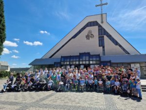 Zdjęcie grupowe podopiecznych oraz pradziejów szkoły życia wraz z duszpasterzem , w tle kościół.