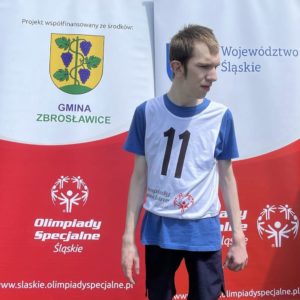 Uczestnik zawodów nordic walking pozujący na tle rollupów z logo miast wspierających wydarzenie.