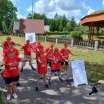 Grupa sportowców podczas rozgrzewki z kijami nordic walking w plenerze.